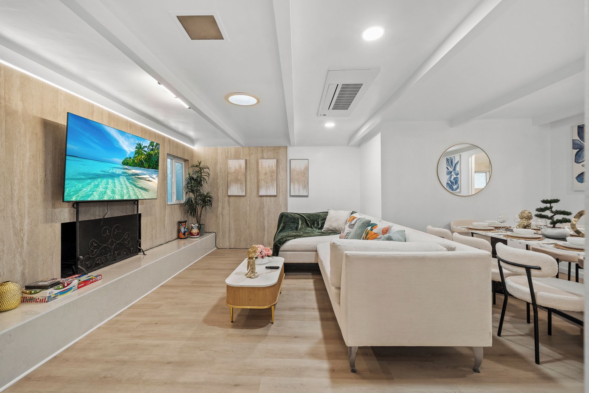 A modern living room with a flat-screen TV, a sofa, a dining area, and a fireplace.