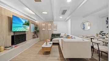 A modern living room with a flat-screen TV, a sofa, a dining area, and a fireplace.
