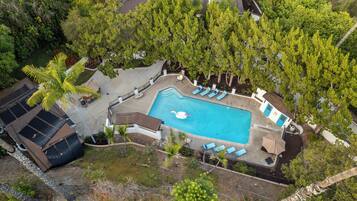 An aerial view of a residential property with a swimming pool, lounge chairs, and surrounding greenery.
