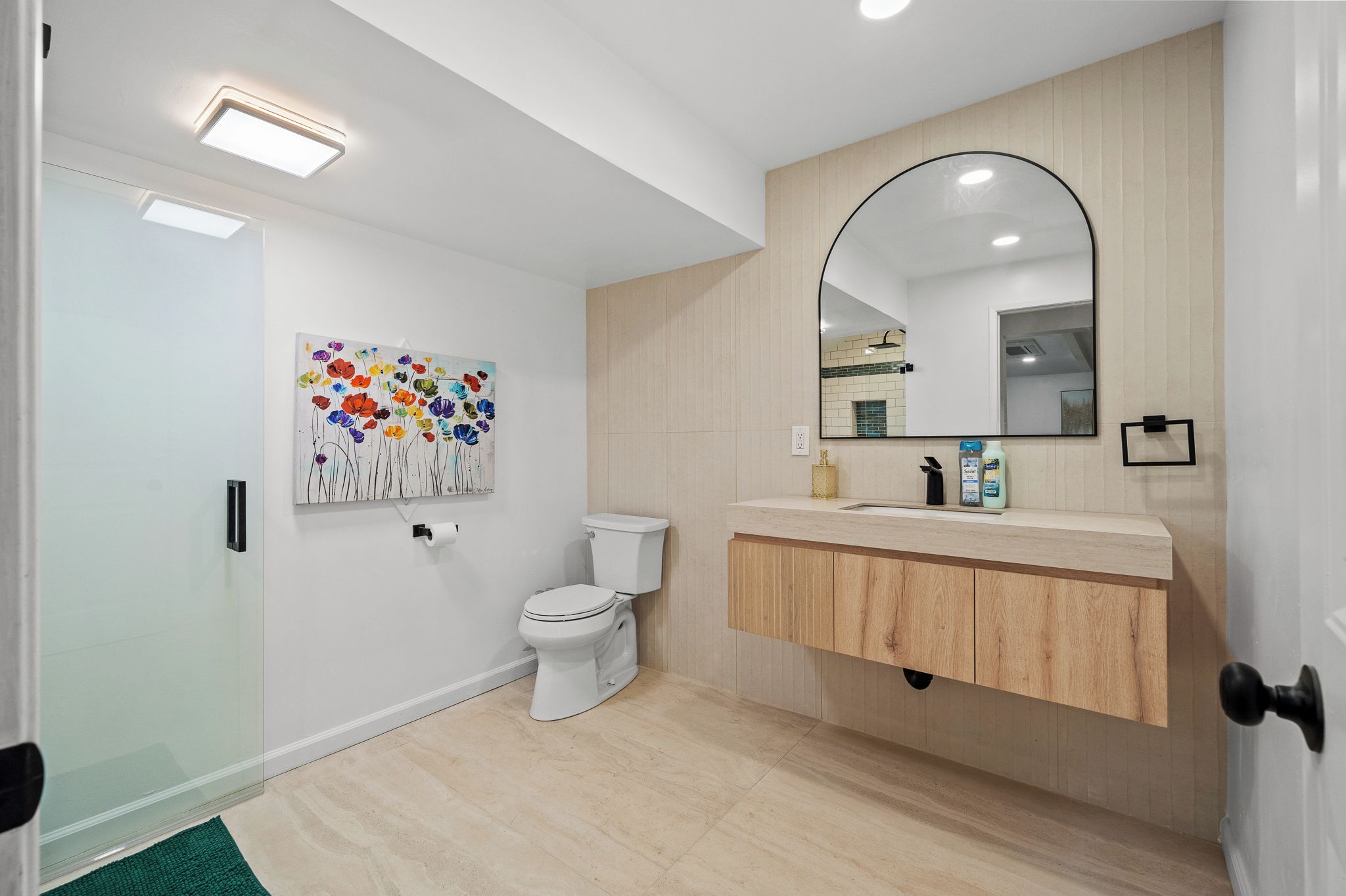 Een moderne badkamer met toilet, een wastafel met spiegel en een kunstwerk aan de muur.