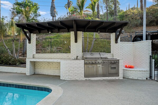 An outdoor kitchen with a grill, oven, and a covered seating area.