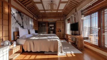 A traditional Japanese-style bedroom with tatami flooring, a large bed with white bedding, a television, and a view of the city through large windows.