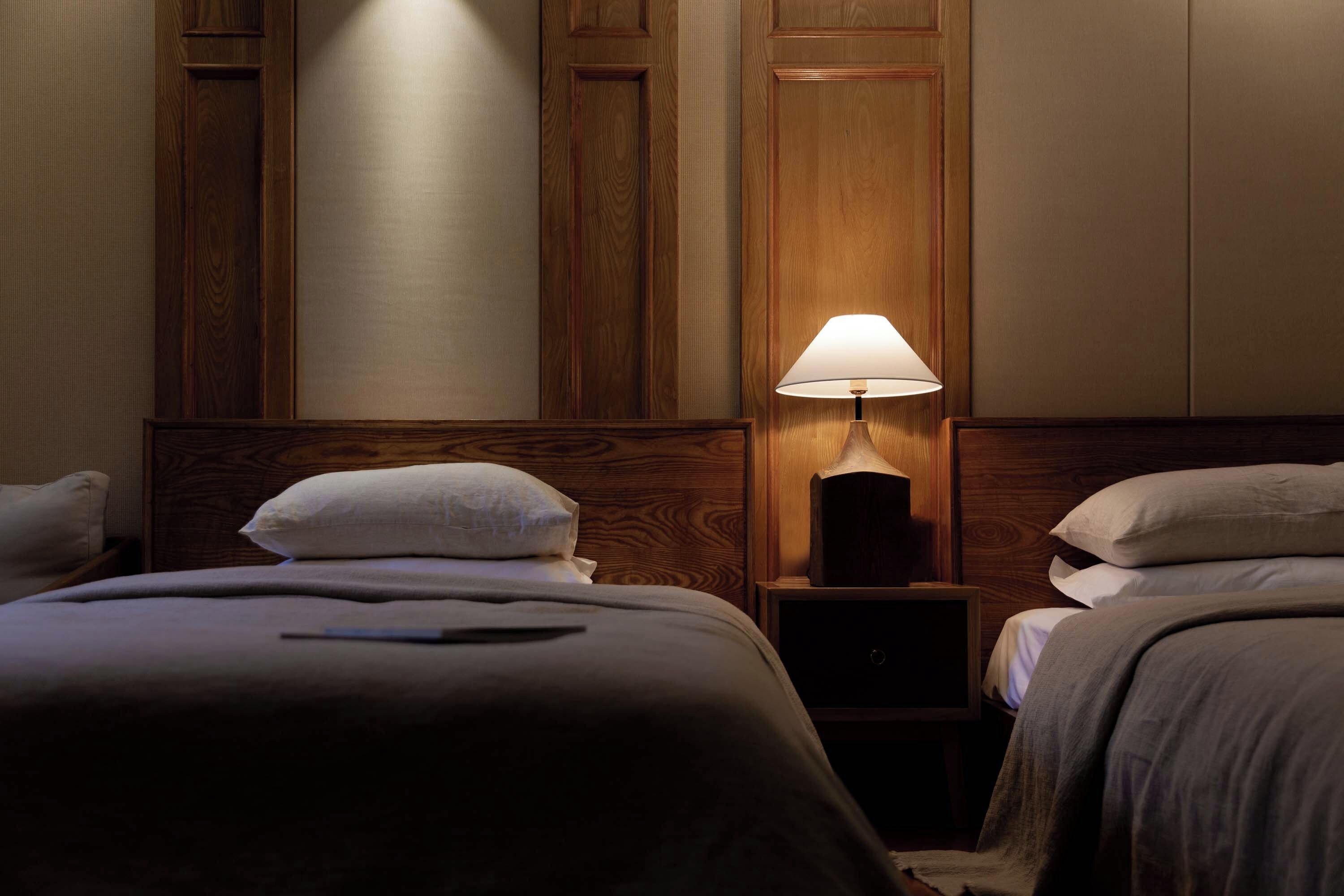 A hotel room with two beds, a nightstand with a lamp, and wooden paneling on the walls.