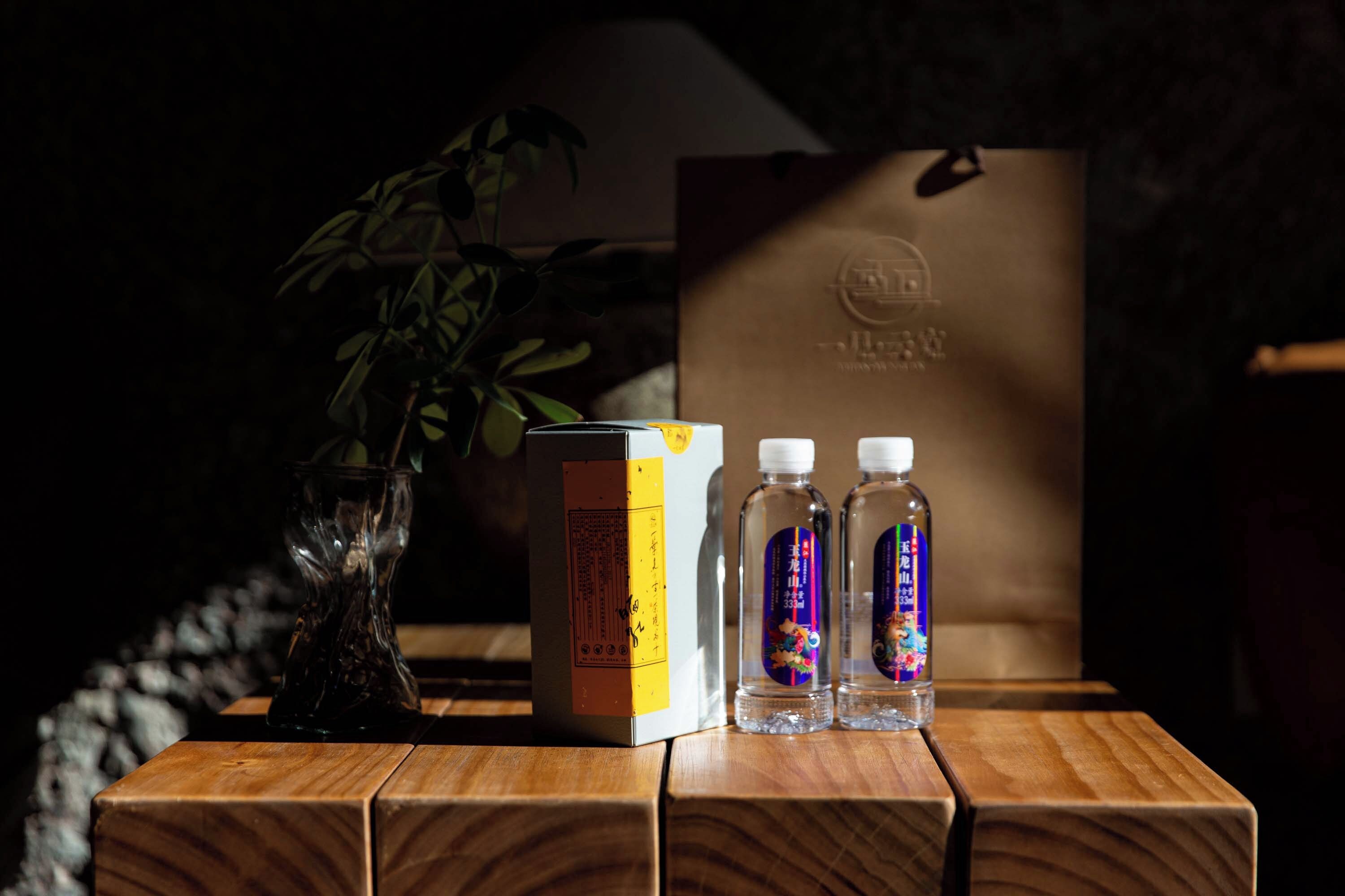 A wooden table with a box, two bottles, and a plant.