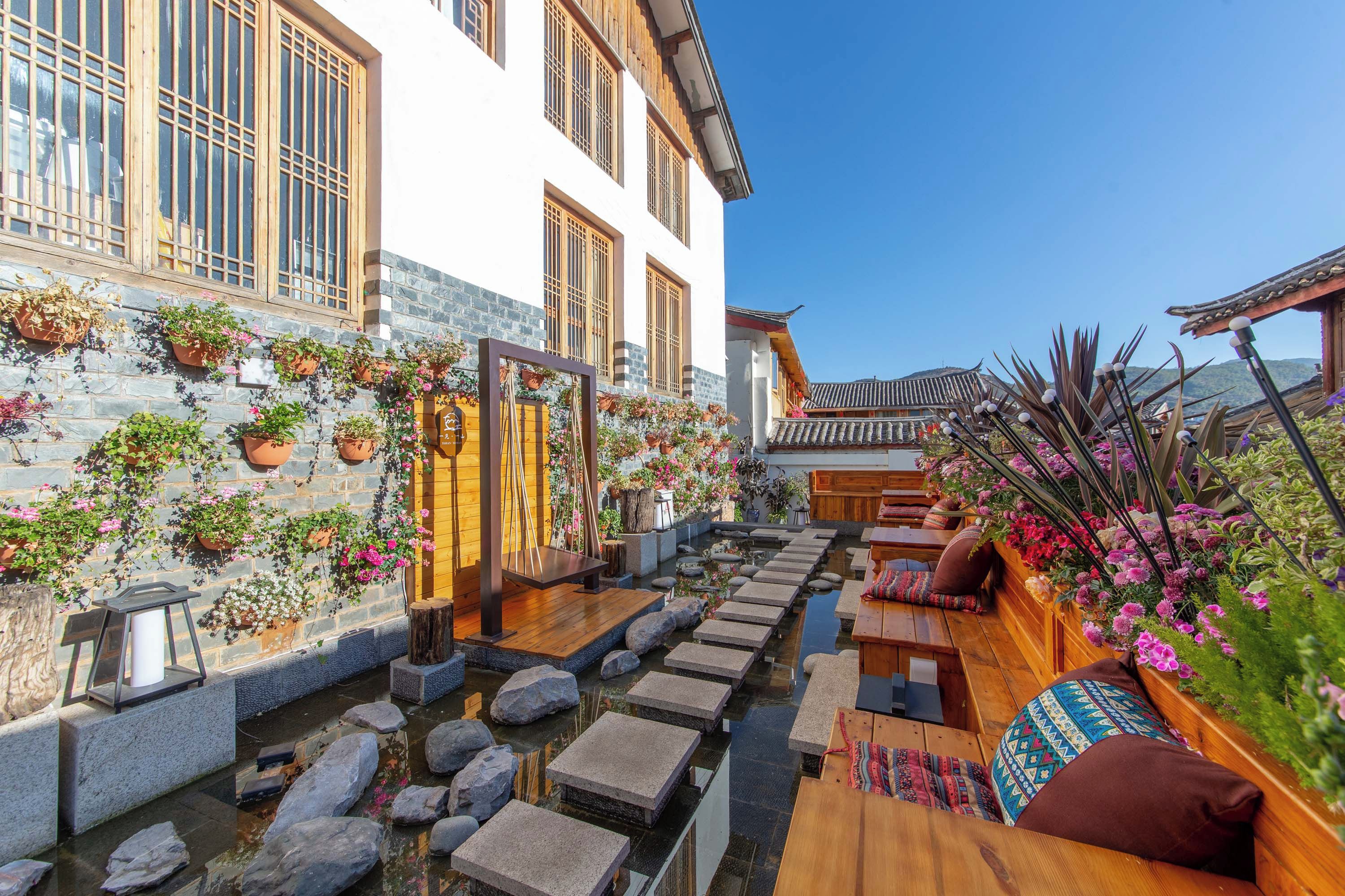 A traditional courtyard with stone steps leading to a wooden bench area, surrounded by potted plants and a small water feature.