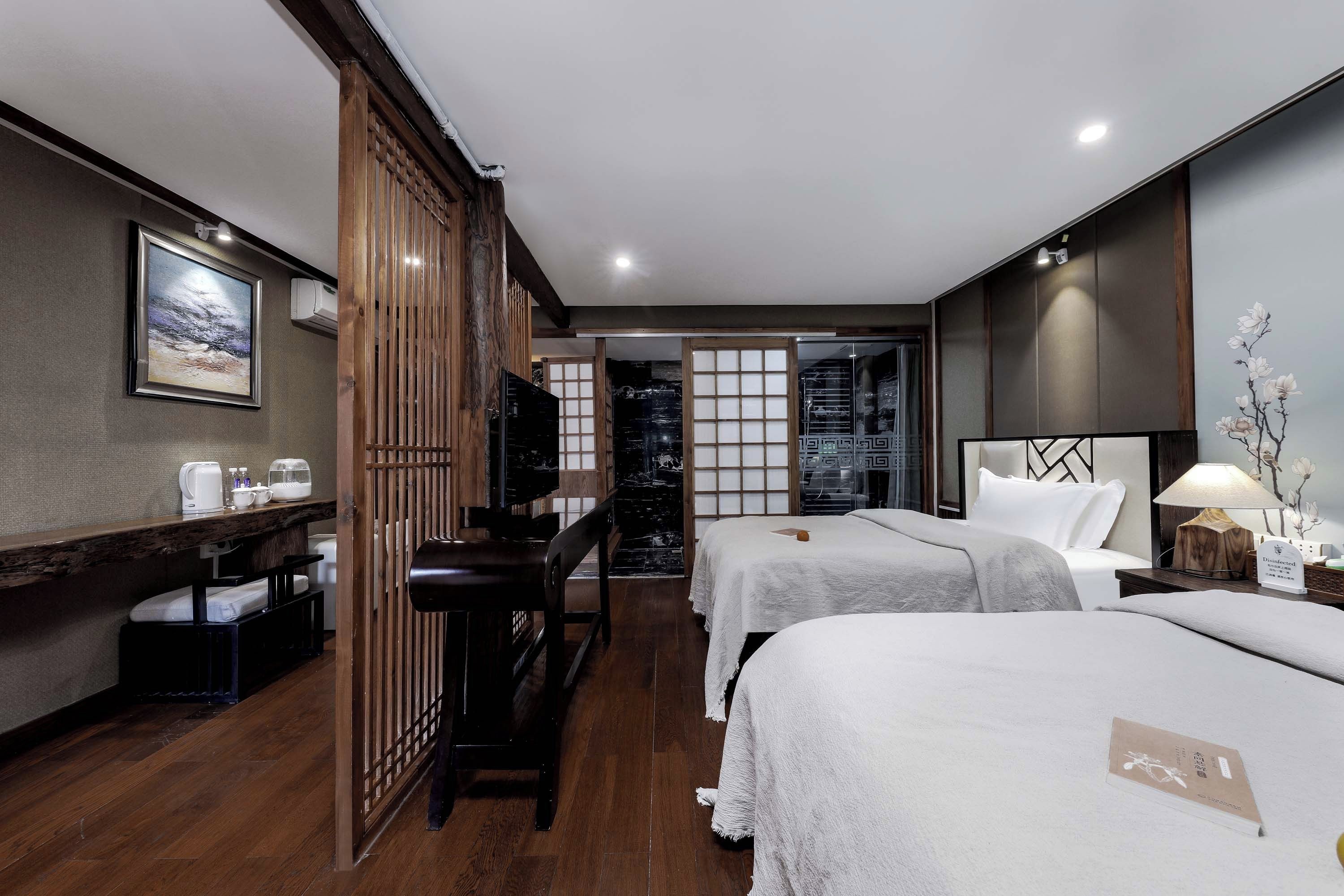 A hotel room with two beds, a desk, a chair, a TV, and a view of a traditional Japanese room.