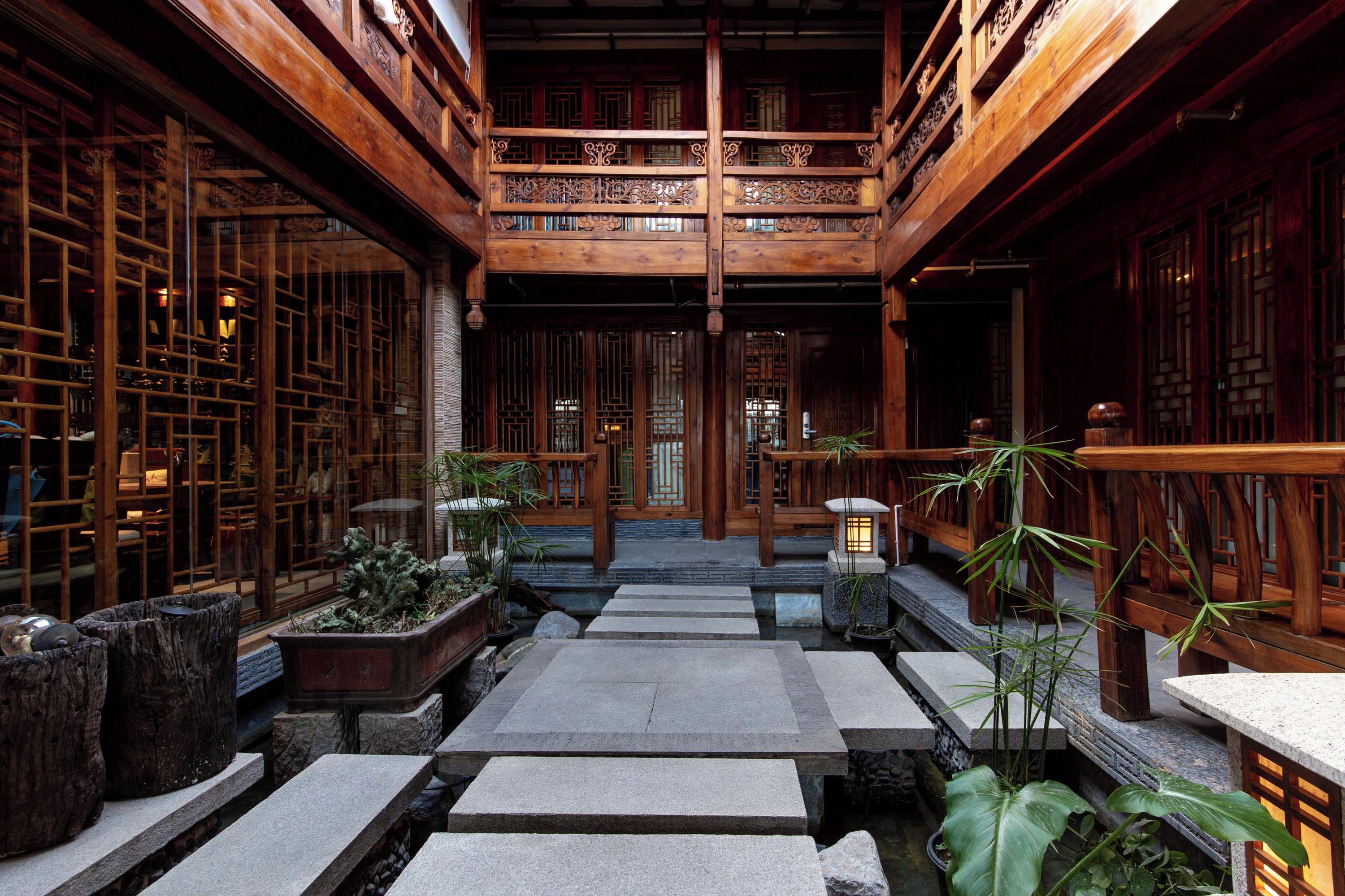 A traditional wooden building with a central courtyard, stone pathways, and potted plants.