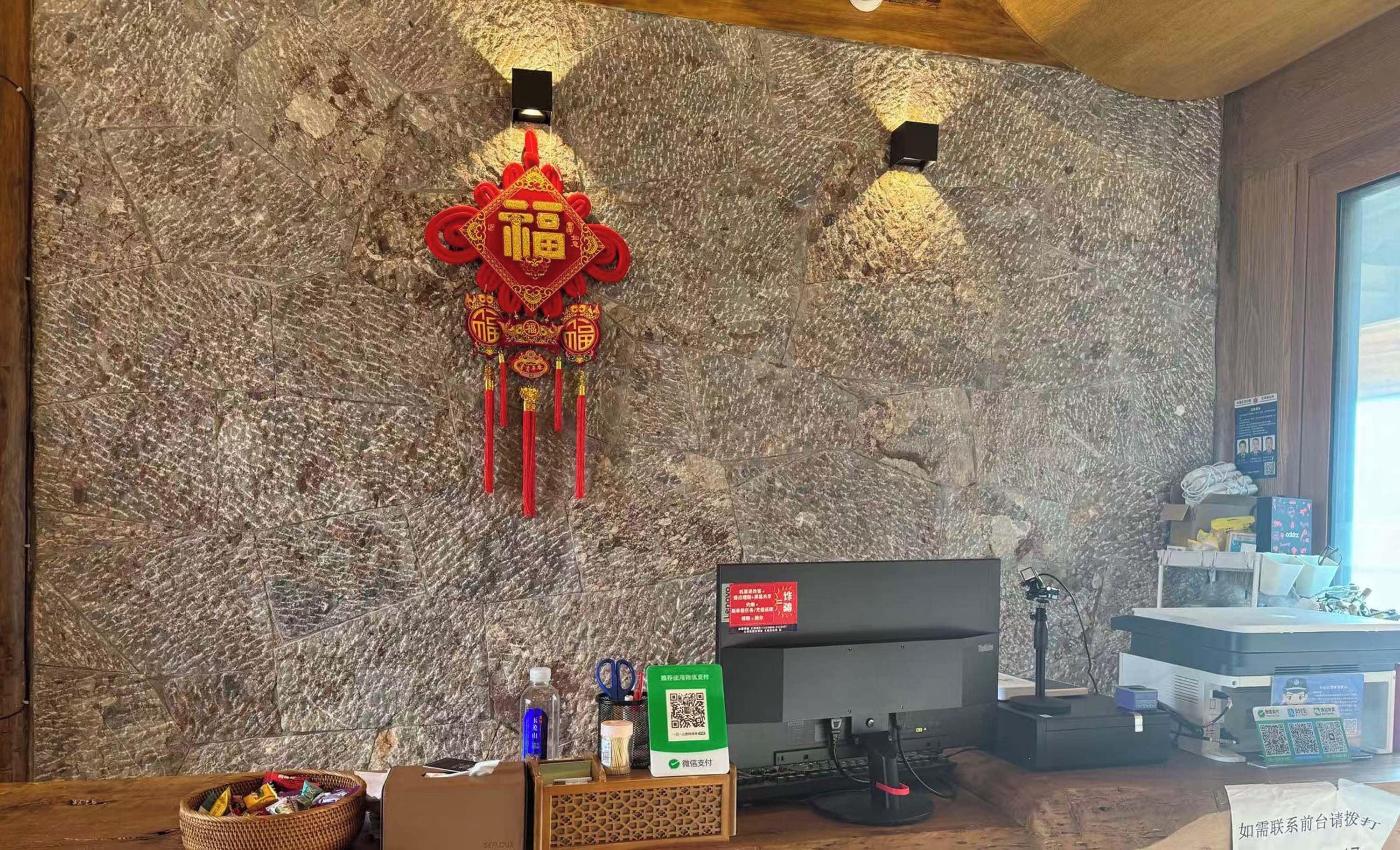 Una habitación con pared de mármol, un adorno colgante rojo, un escritorio con ordenador y un soporte para código QR.