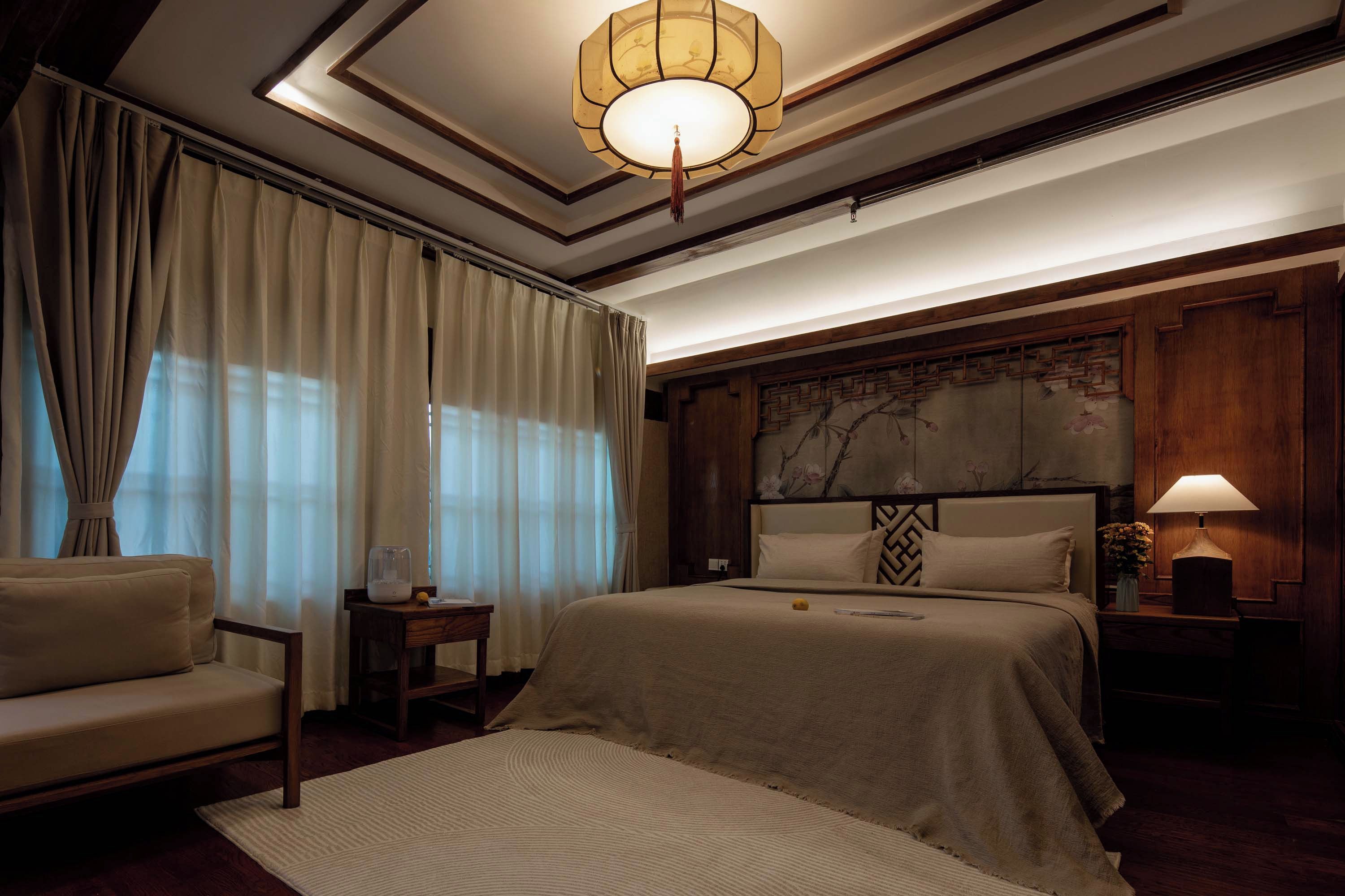 A hotel room with a large bed, a bedside table, a lamp, and a view of the outdoors.