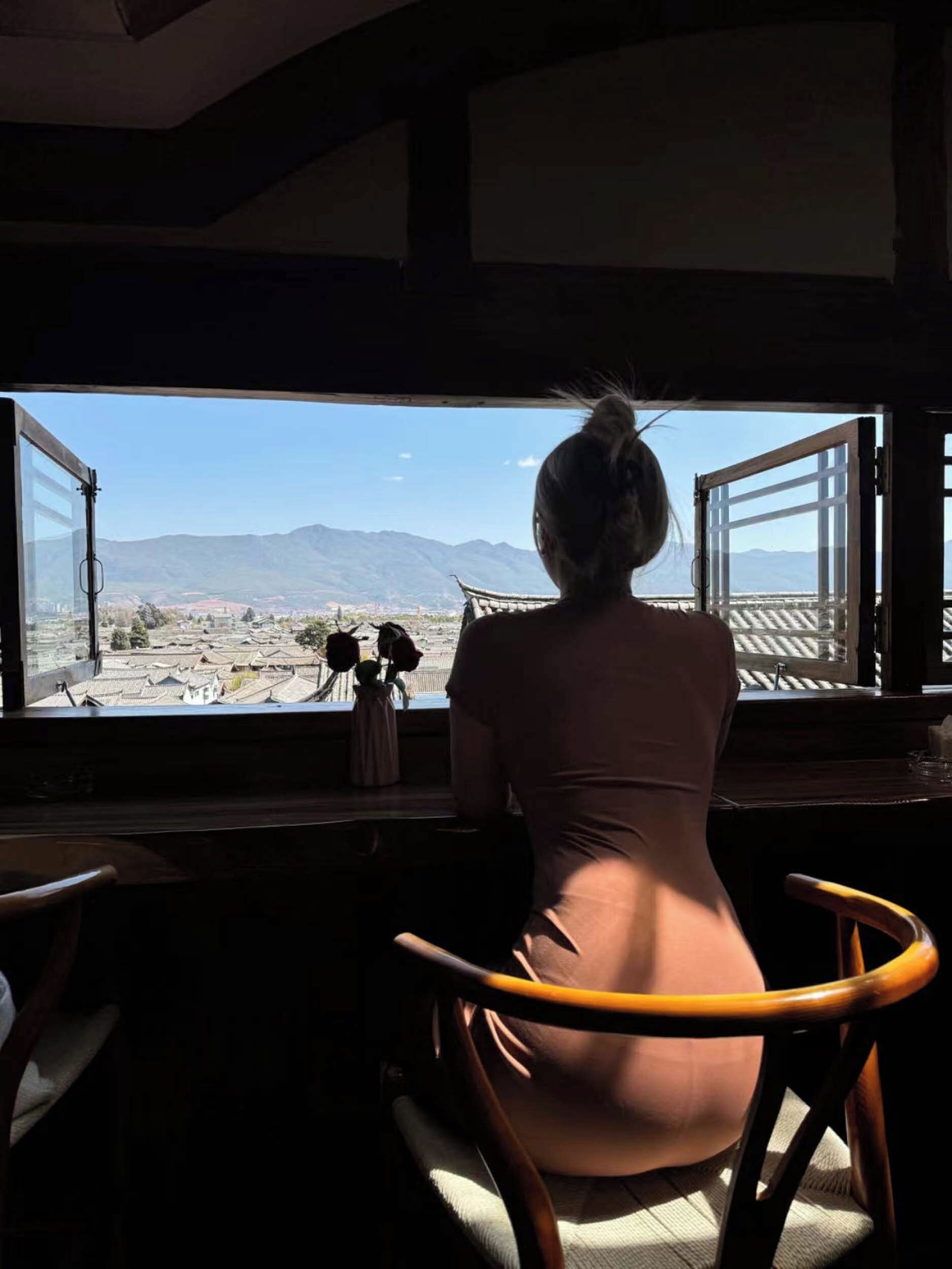 A person seated by a window with a view of a mountainous landscape.