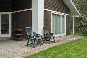 A patio area with two chairs and a small table, a wooden bench, and a window with curtains. - Cozy holiday home with spa and sauna (Rødby)