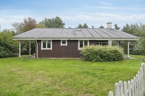 A single-story house with a sloped roof, a fenced yard, and a small garden area. - Cozy holiday home with spa and sauna (Rødby)