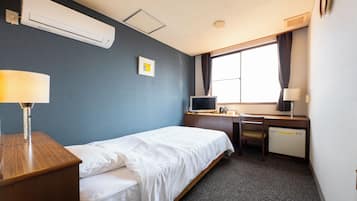 A hotel room with a bed, desk, chair, air conditioning unit, window with curtains, and a wall-mounted picture.