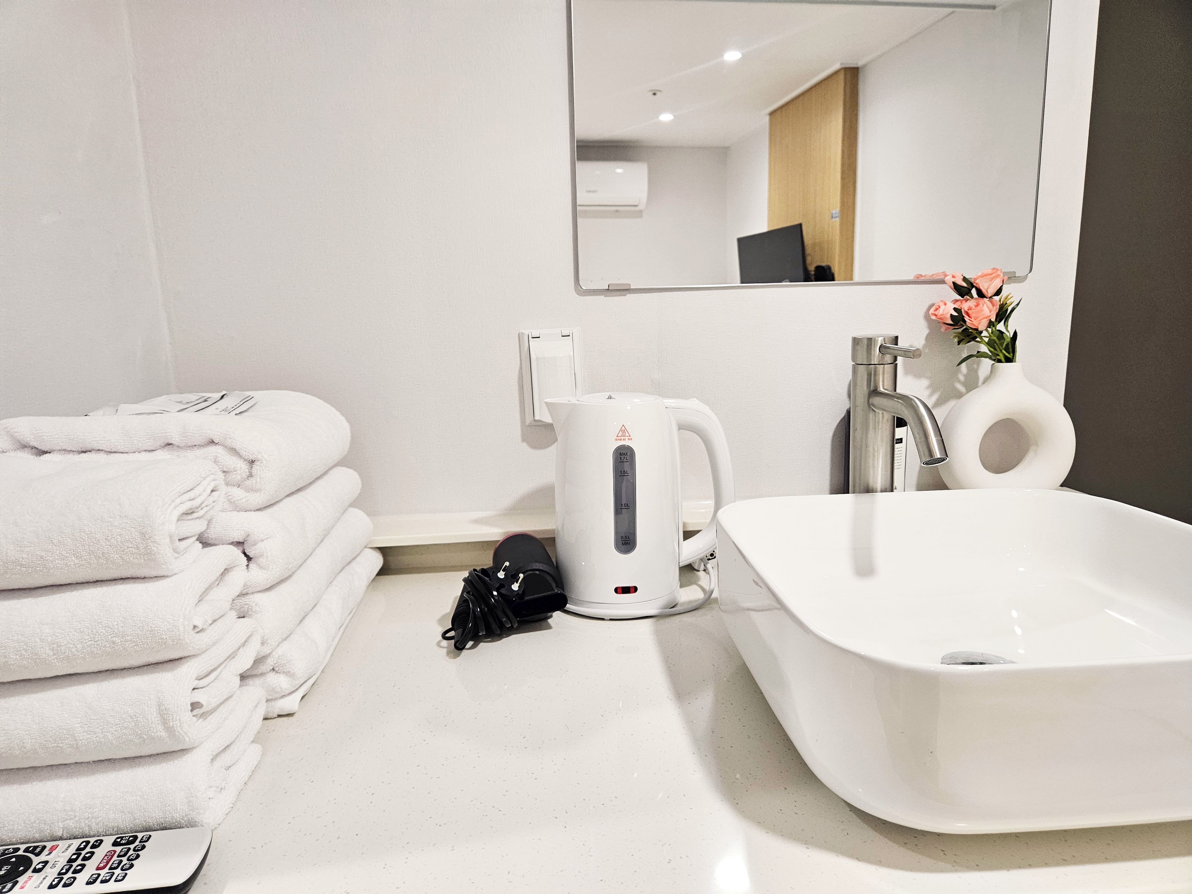 Une salle de bain d’hôtel équipée d’un lavabo, d’un miroir, d’une pile de serviettes et d’une bouilloire.