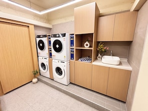 A laundry room with stacked washing machines, a sink, and a shelf with decorative items. - Monolith Stay Hotel (Incheon)