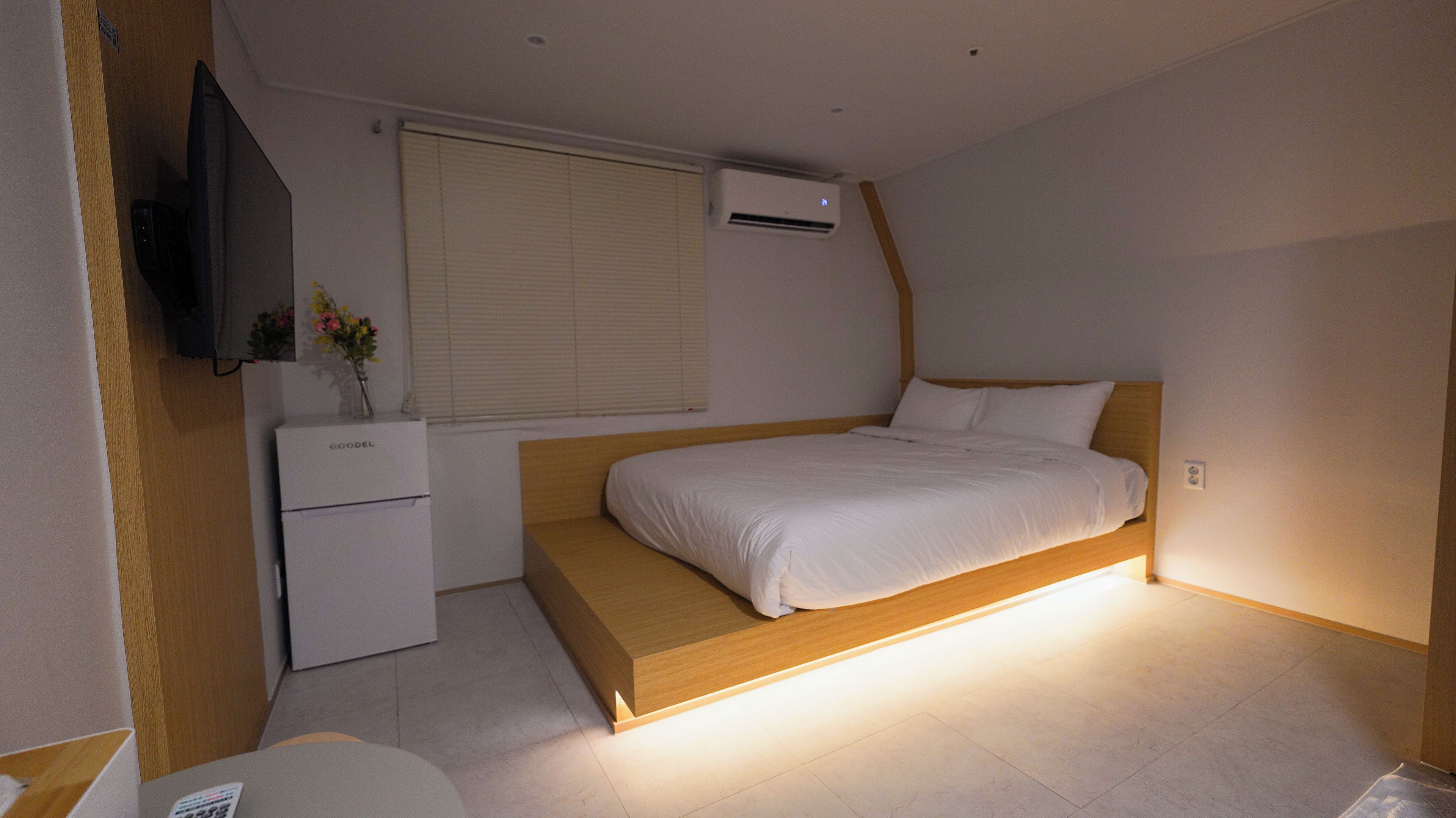 A bedroom with a bed, a bedside table, a TV, and an air conditioning unit.