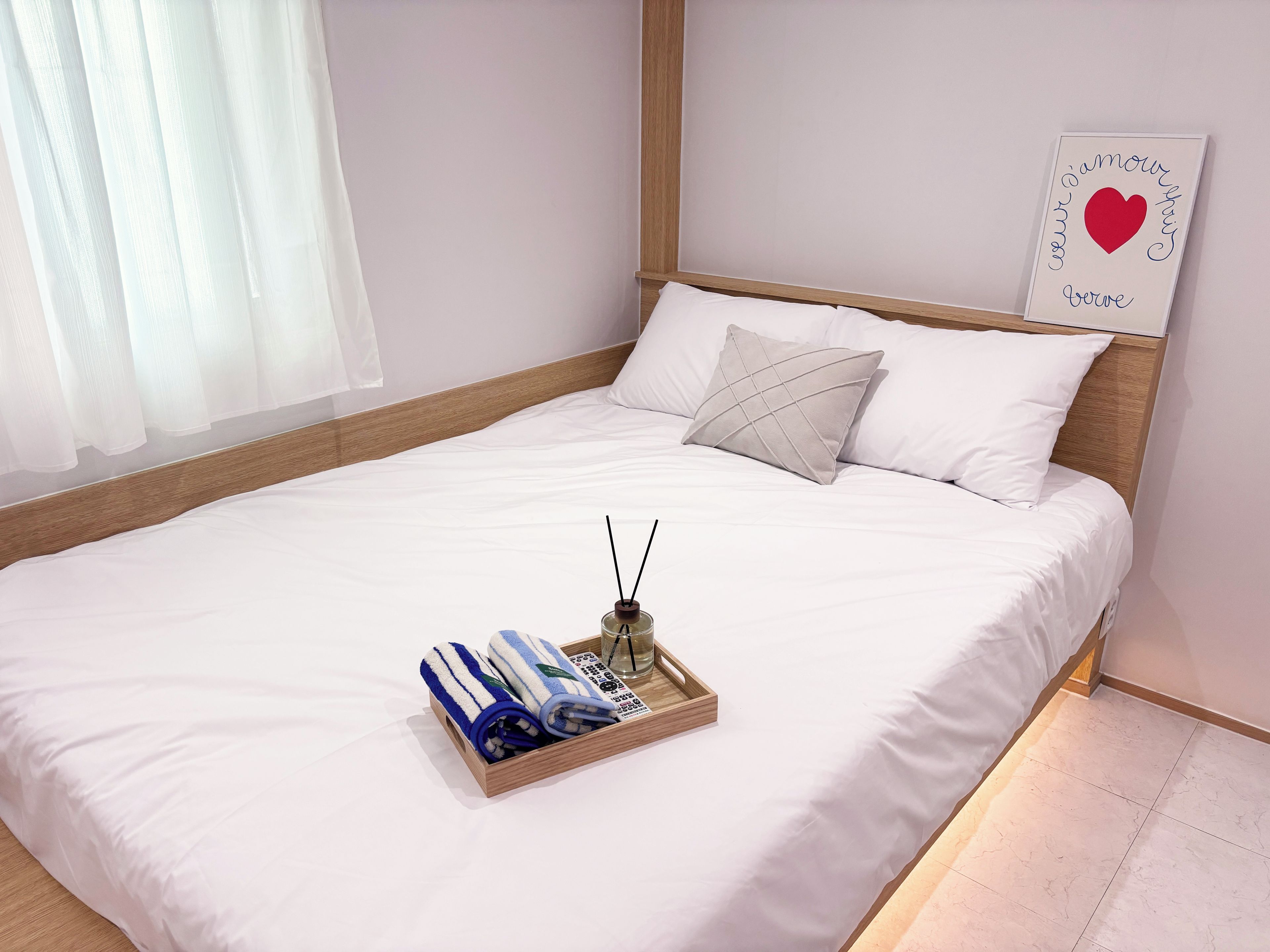 A neatly made bed with white linens, a wooden headboard, and a bedside table with a glass and a blue striped towel.