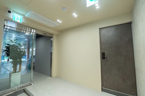 A hallway with a glass door entrance, a door with a handle, and a ceiling with recessed lighting. - Monolith Stay Hotel (Incheon)