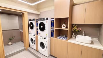 A laundry room with two stacked washing machines, a sink, and a shelf with decorative items.