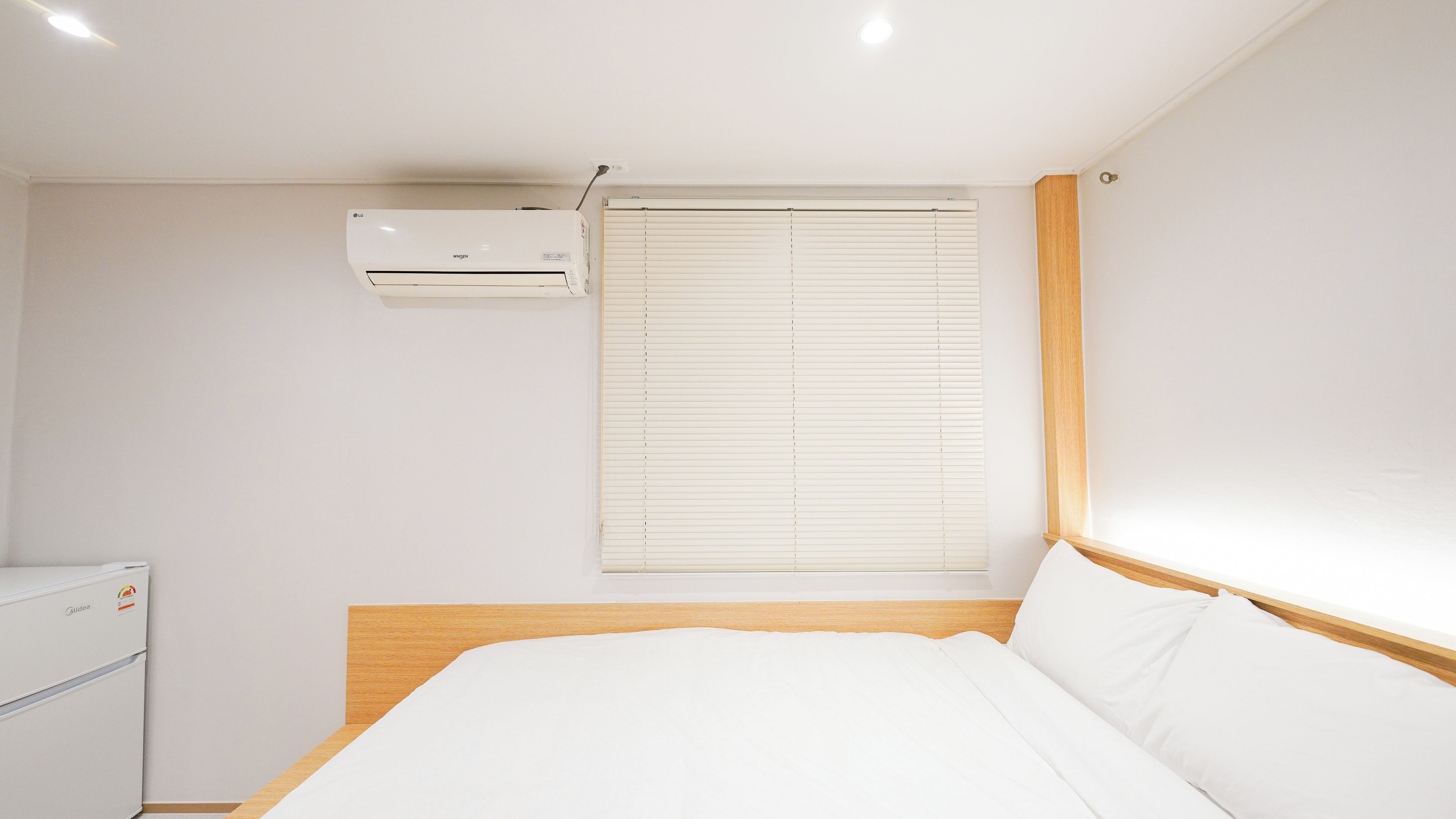 A bedroom with a bed, a window with blinds, an air conditioning unit, and a wooden headboard.