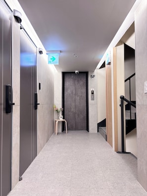 A hallway with an elevator, a directional sign, and a small table with flowers. - Monolith Stay Hotel (Incheon)