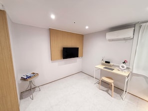 A modern, minimalistic room with a flat-screen TV mounted on the wall, a small desk with a chair, and an air conditioning unit. - Monolith Stay Hotel (Incheon)