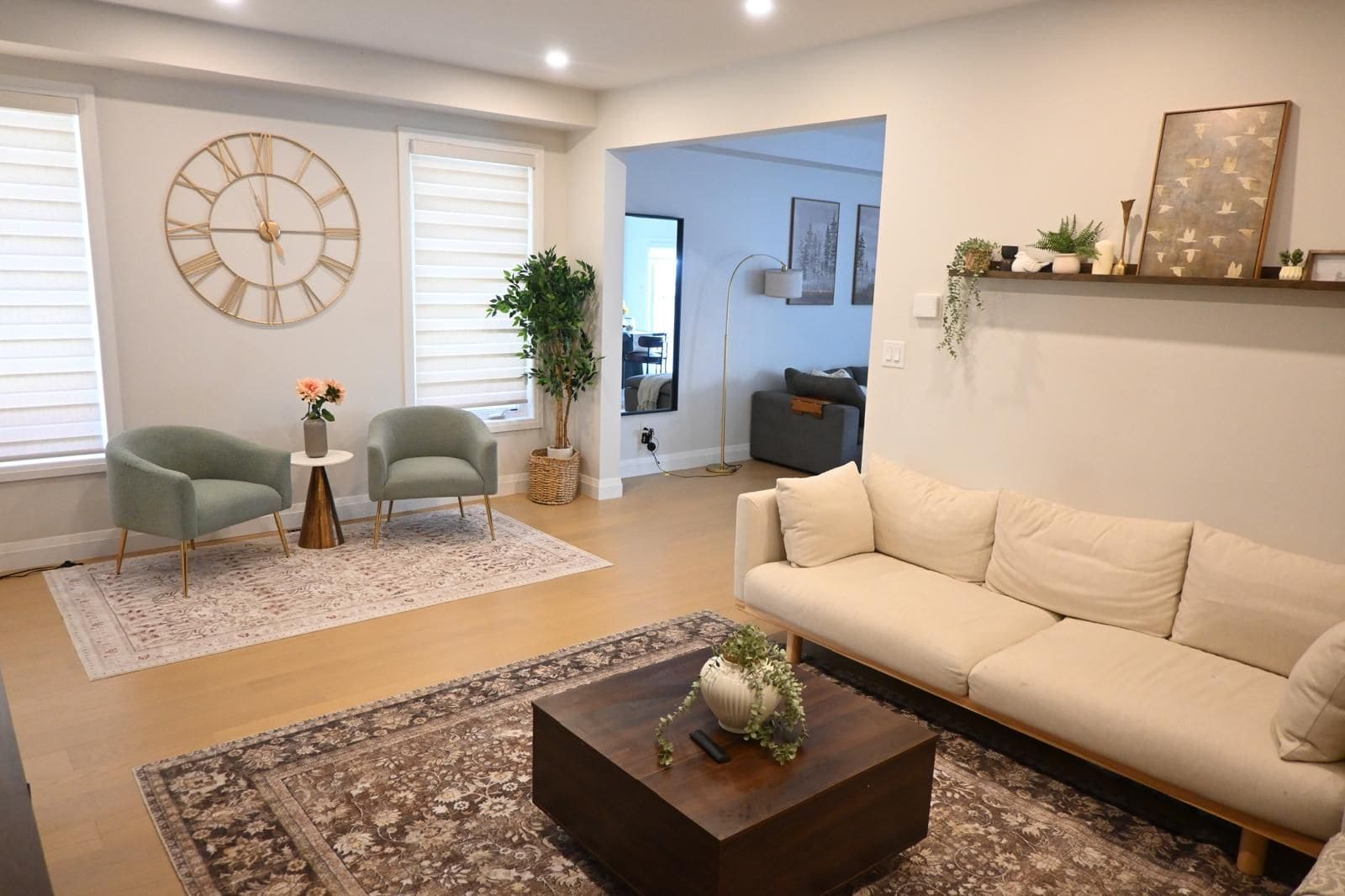 Un salon comprenant un canapé, deux fauteuils, une table basse, une grande horloge murale et une plante.