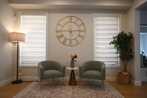 A room with two armchairs, a round wall clock, a small table with flowers, and a potted plant. - Modern 4 bedroom house in Milton (Milton)