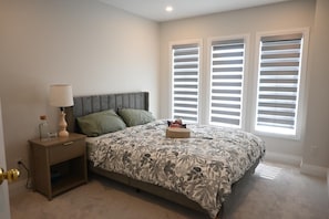 A bedroom with a bed, nightstand, lamp, and window blinds. - Modern 4 bedroom house in Milton (Milton)