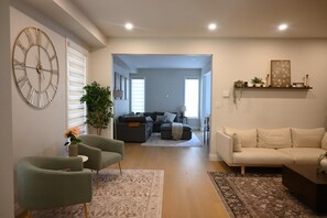 Ein Wohnzimmer mit einer Couch, Sesseln, einem Couchtisch und einer dekorativen Uhr an der Wand.