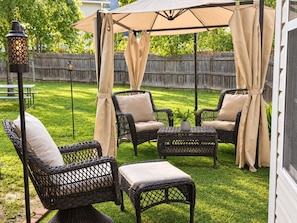 Eine Terrasse mit Korbmöbeln, einem Tisch und einer Pergola mit Vorhängen.