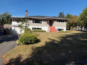 A two-story house with a garage, a covered porch, and a small front yard. - Spacious 3 Bedroom, 2 Bathroom Basement Suite – Central Coquitlam (Coquitlam)
