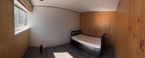 Habitació petita amb un llit individual, panells de fusta a les parets i una finestra que deixa entrar llum natural.