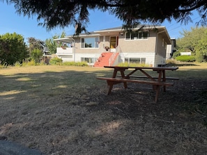 Ein zweistöckiges Haus mit einer überdachten Veranda, einer Treppe, die zu der oberen Etage führt, und einem Picknicktisch im Garten.