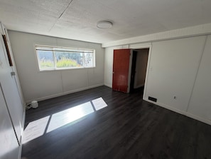 A room with a large window, wooden flooring, and a door leading to another room. - Spacious 3 Bedroom, 2 Bathroom Basement Suite – Central Coquitlam (Coquitlam)