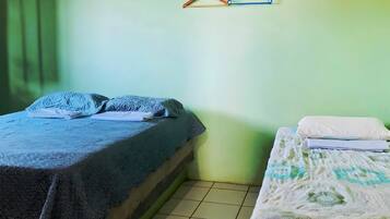 Duas camas de solteiro com estilos de roupa de cama diferentes, um cabide fixado na parede e piso ladrilhado.
