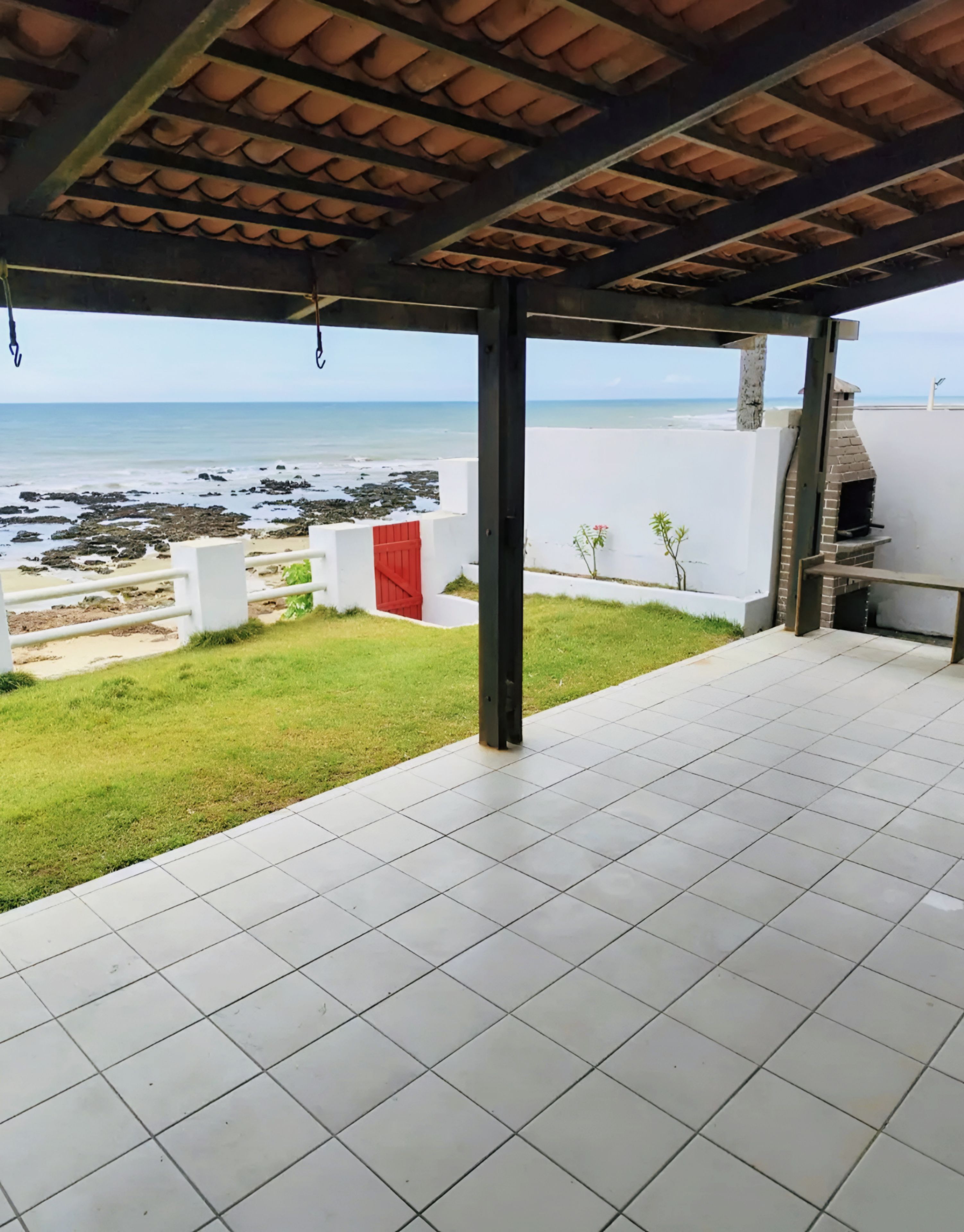 A covered patio with a view of the beach and rocky shoreline.