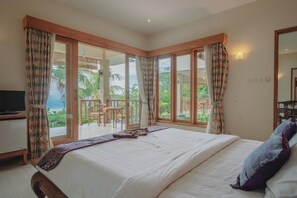 Ein Schlafzimmer mit einem großen Bett, einem Fernseher und einem Balkon mit Blick auf Palmen.