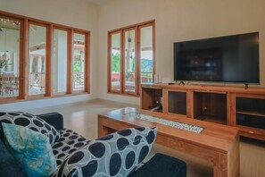 Ein Wohnzimmer mit einem großen Flachbildfernseher, Holzmöbeln und großen Fenstern.