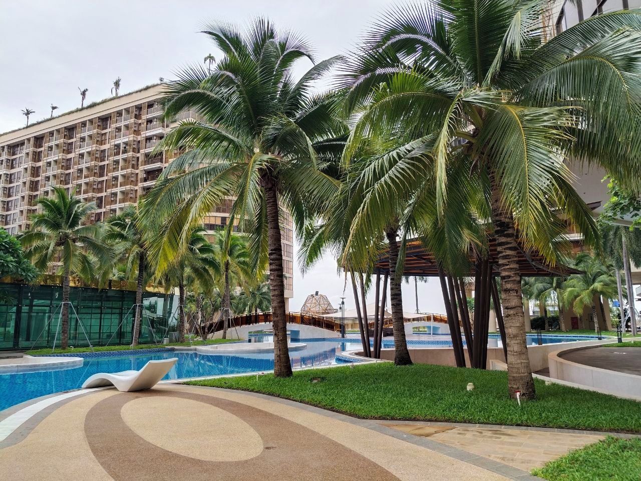 A hotel with a swimming pool surrounded by palm trees and a large building in the background.