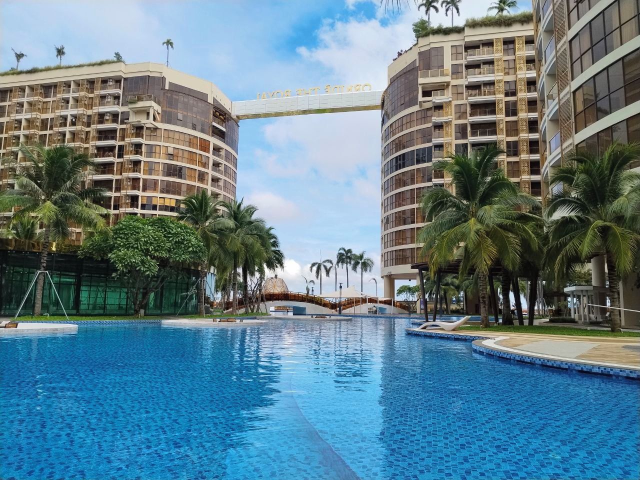 Un hôtel doté d’une grande piscine, entourée de palmiers et bordée de bâtiments modernes.