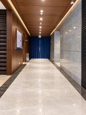 A modern hallway with a wooden ceiling, marble flooring, and a blue curtain at the end.