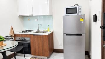 A compact kitchen with a gas stove, a microwave, and a stainless steel refrigerator.