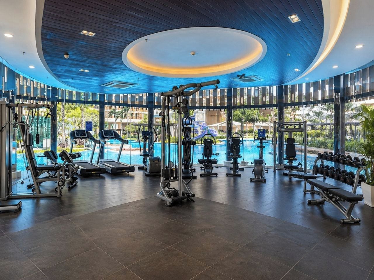 A gym with exercise equipment, a swimming pool, and large windows.