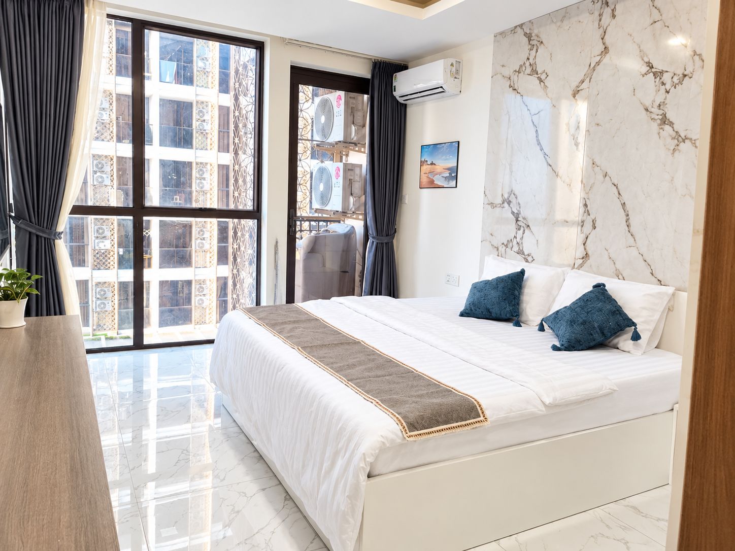 A hotel room with a large bed, a marble wall, and a view of buildings outside.