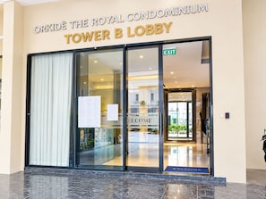 The entrance to the Royal Condominium Tower B Lobby with a glass door, an exit sign, and a welcome mat.