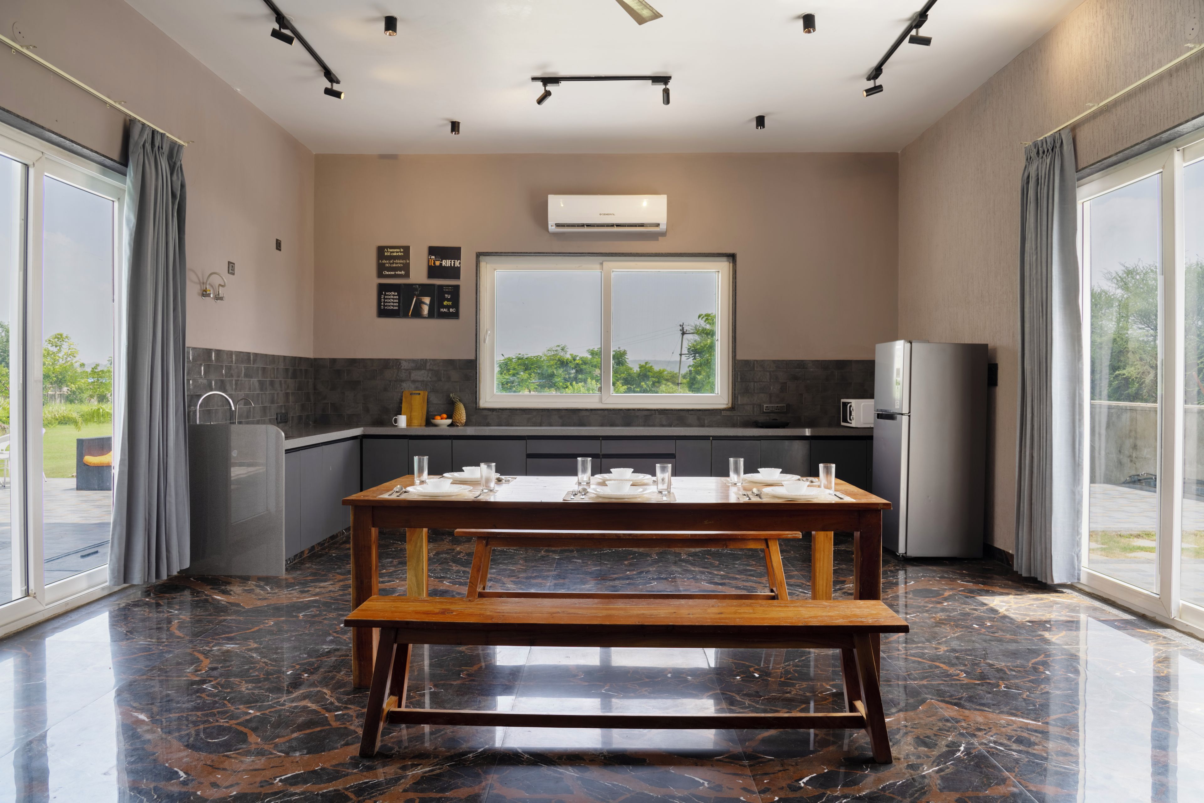A modern kitchen with a dining area, large windows, and a view of greenery.