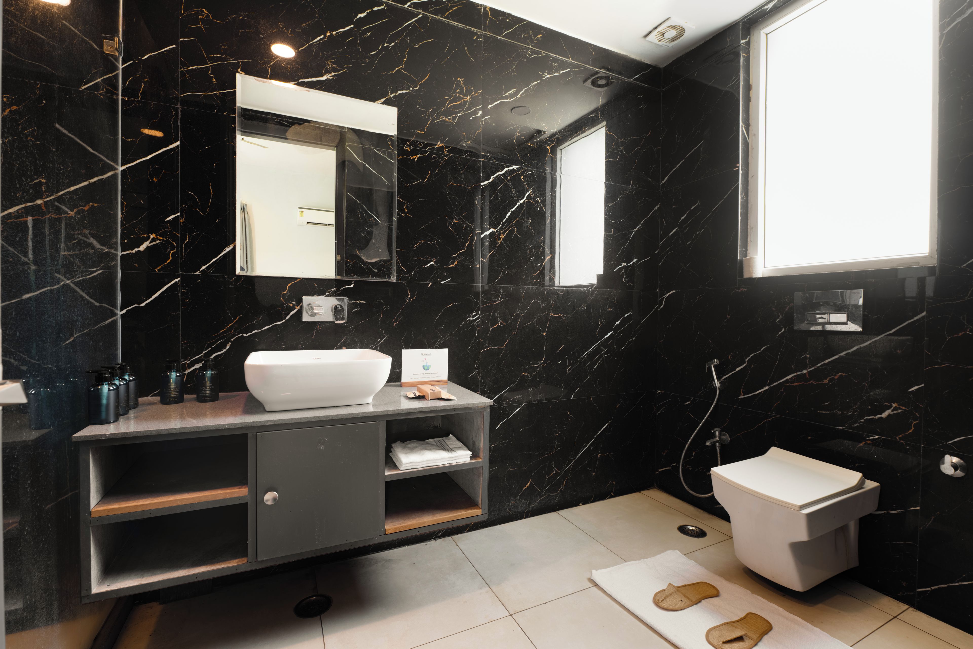 Une salle de bain moderne avec un mur en marbre noir, un lavabo blanc, un miroir et des toilettes.