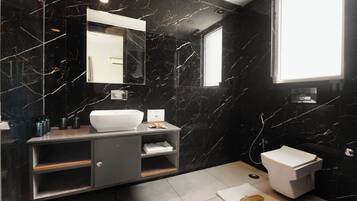 Une salle de bain moderne avec un mur en marbre noir, un lavabo blanc, un miroir et des toilettes.