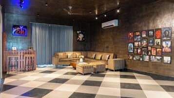 Un salon moderne avec un sol à carreaux, un ensemble de canapés, une table basse, un coin bar avec des tabourets et un mur décoré d’affiches de films.